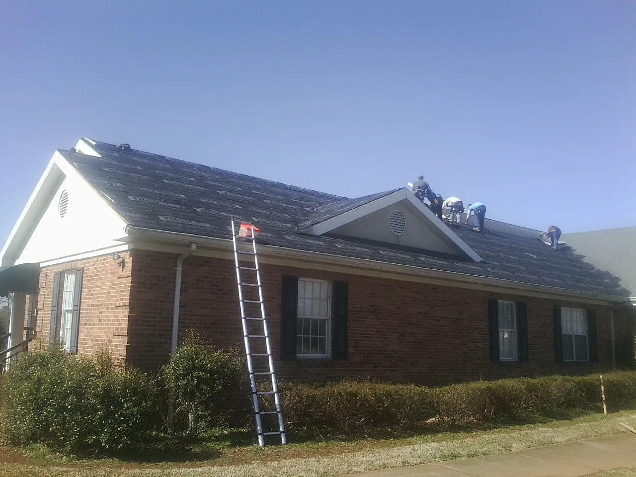Crew tearing shingles off a brick ranch roof with a ladder set — Metal Roof Repair work by our crew in Elizaville