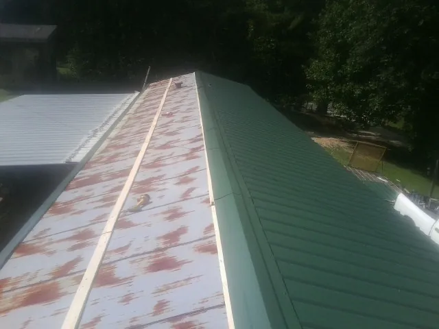 Old rusted panels beside newly installed green metal roofing — Wind Damage Roof Repair by Roofing Brothers in Elizaville