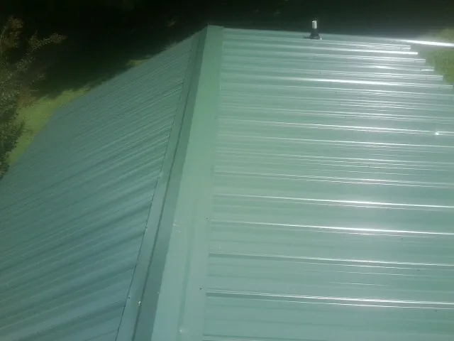 New green metal panels meeting at the ridge of a roof — Flat Roof Repair work by our crew in Elizaville