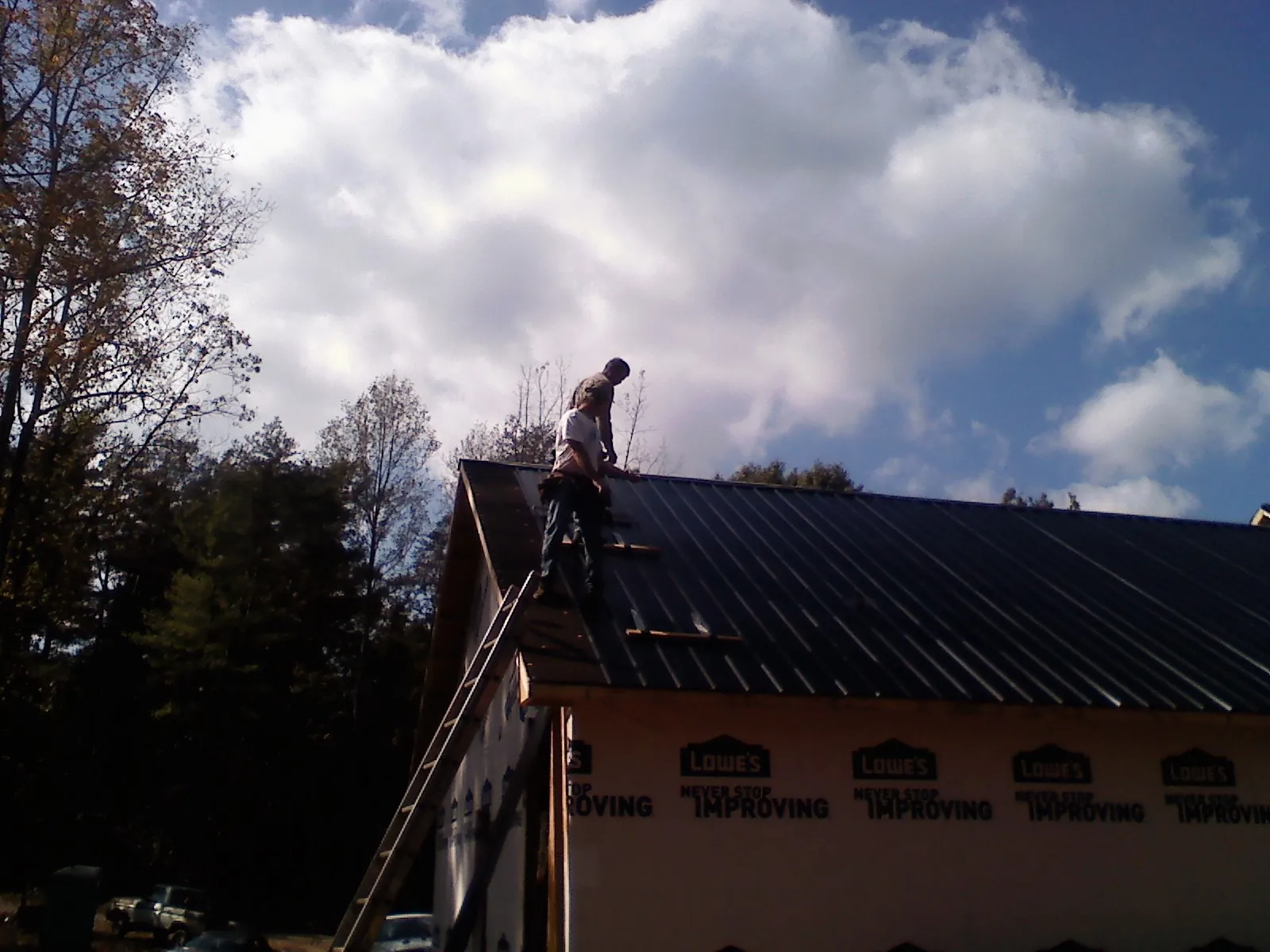 Roofer fastening dark metal panels high against a cloudy sky, from a Roof Inspection job in Elizaville