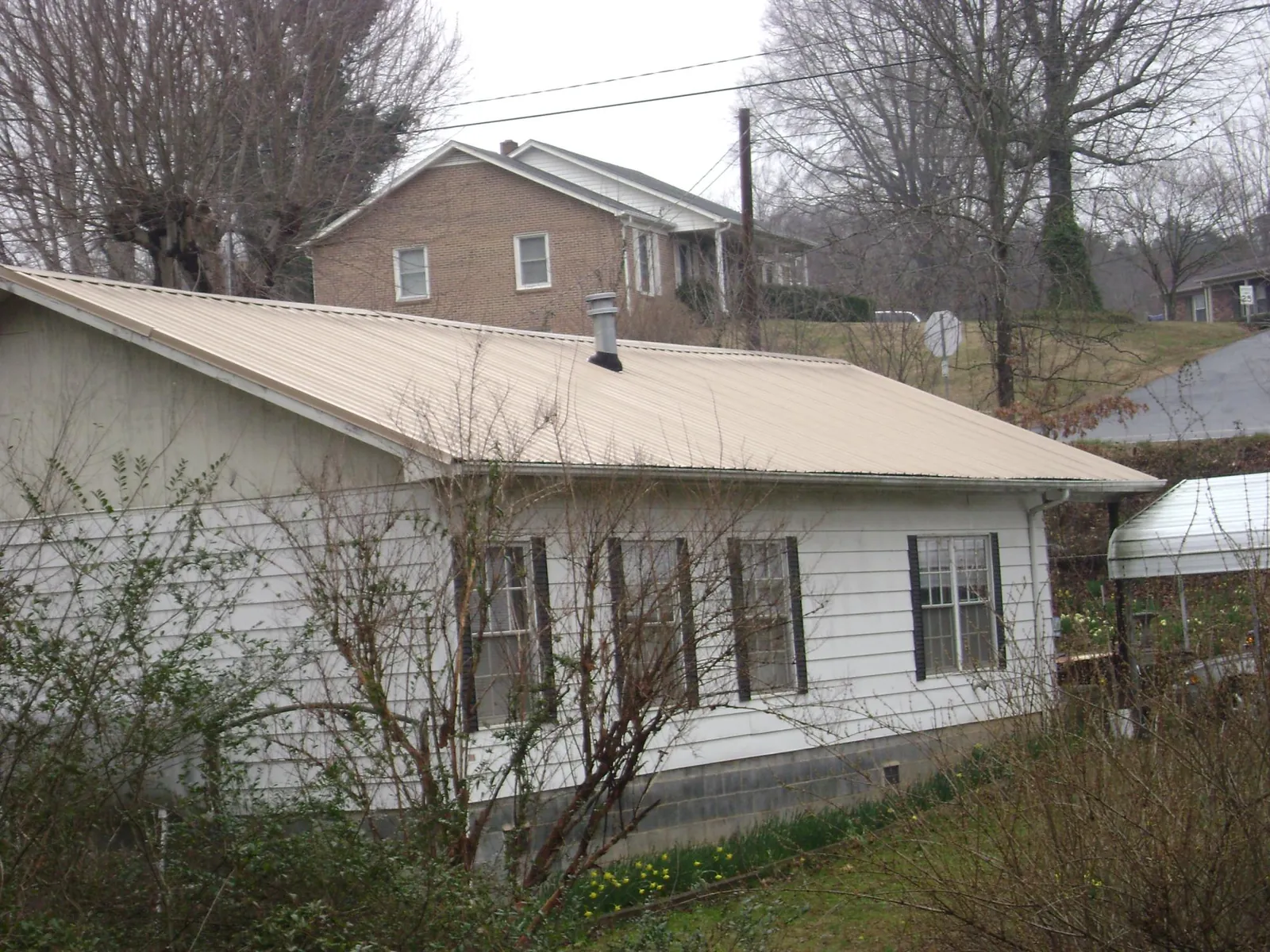 Tan metal roof on a white sided house set into a hillside — Commercial Roofing by Roofing Brothers in Elizaville