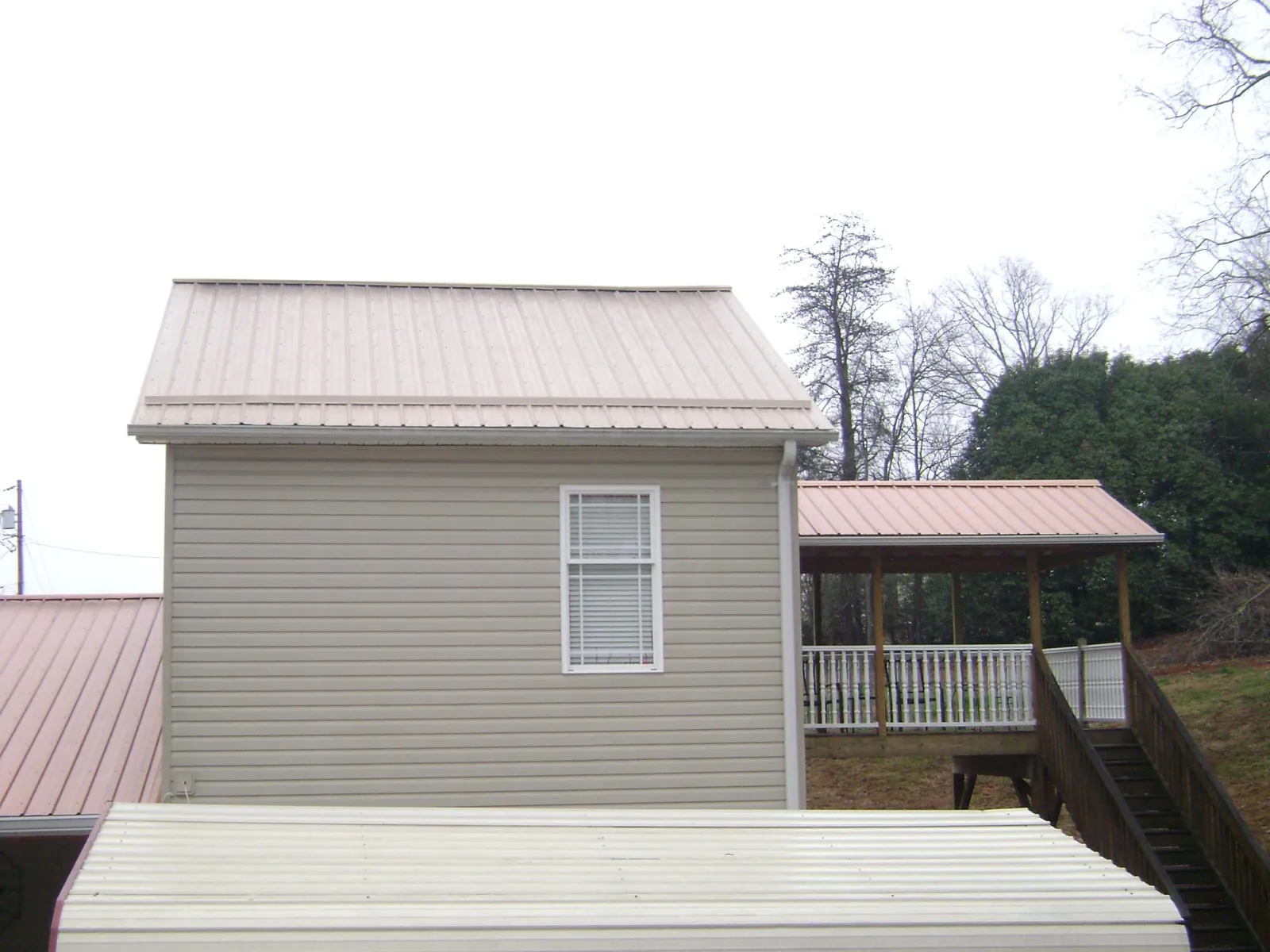 Tan metal roofs on a two story addition and attached porch, from a Roof Replacement job in Elizaville